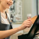 Cute female cashier holding credit card near monitor